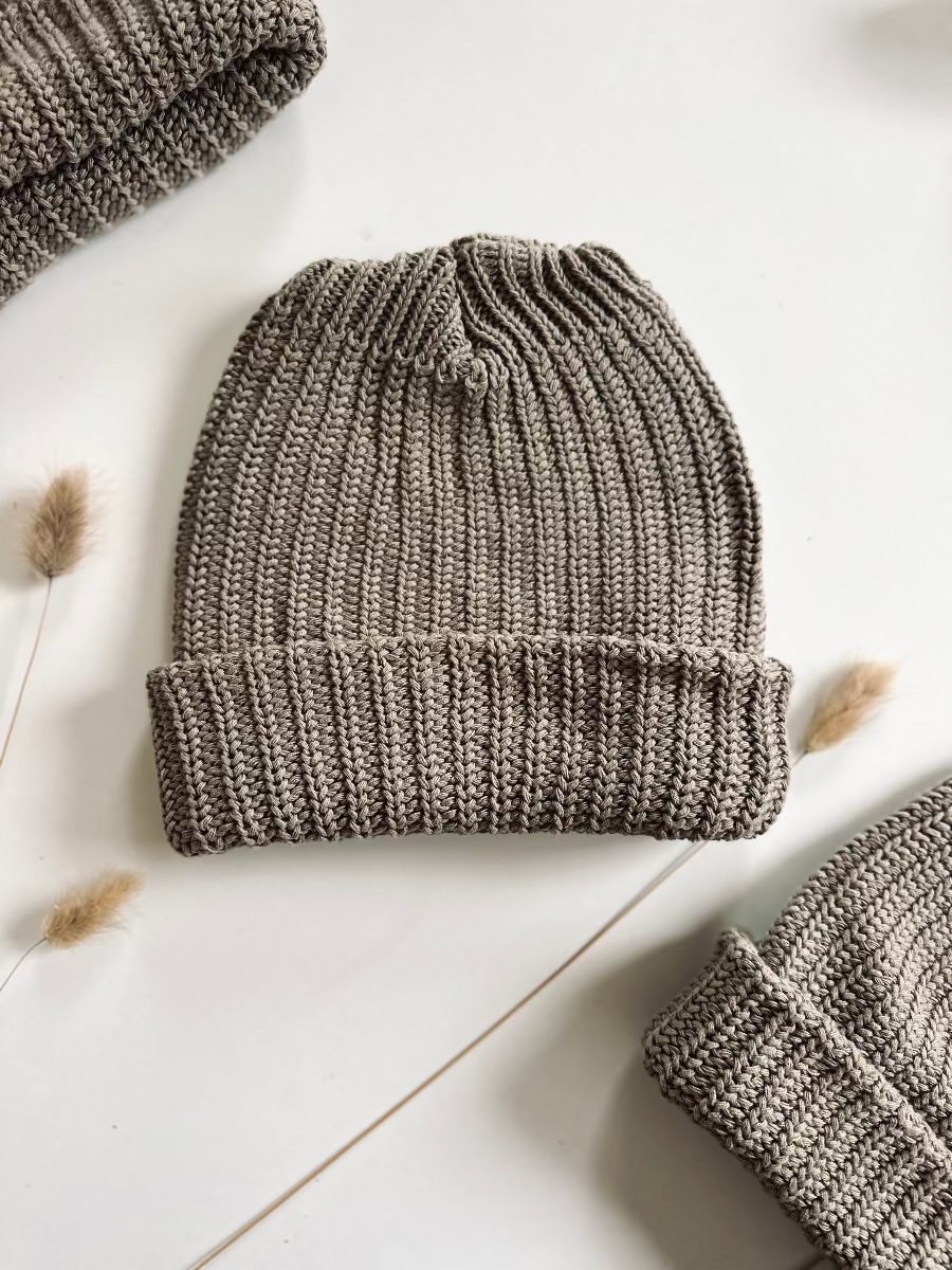 chunky knit beanie hat brow/ gray/ mushroom on a light wooden surface with dried plants.