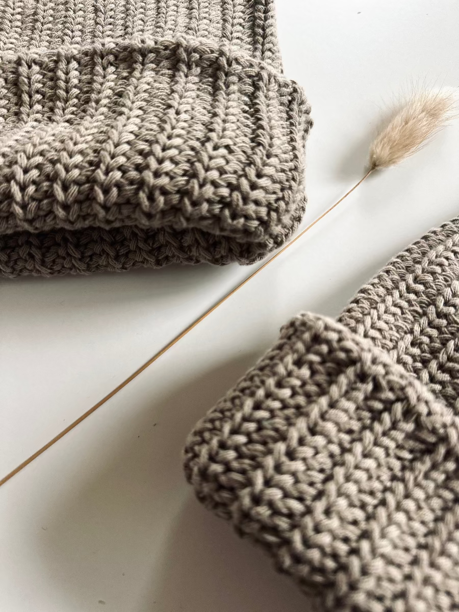 Two chunky knit beanie hats gray brown folded knitted items on a light wooden surface