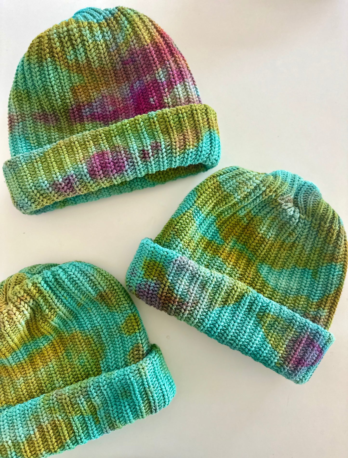 Three chunky knitted tie-dye hats with a multicolor pattern on a white background